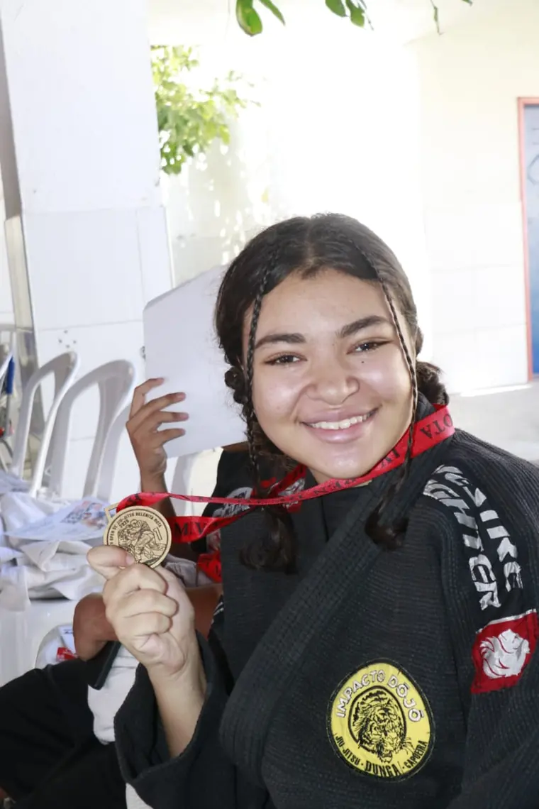 Aluna de kimono preto segurando um certificado e sorrindo