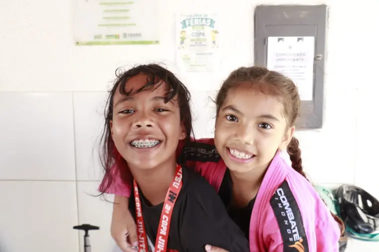 Duas alunas de kimono preto e rosa sorrindo com medalhas