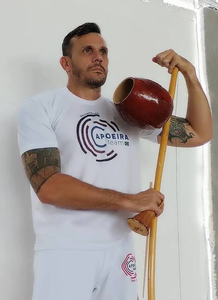 Capoeirista de touca segurando um berimbau, uniforme branco