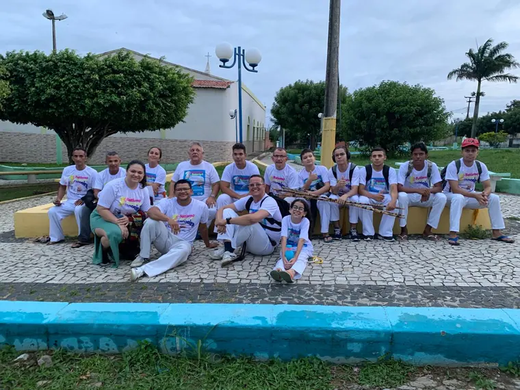 Grupo de capoeiristas reunido em uma praça com fonte ao fundo