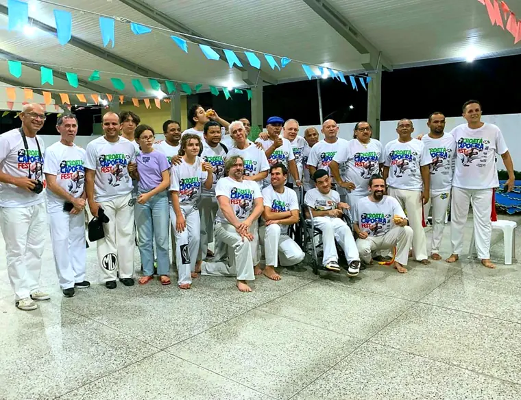 Grande grupo de capoeiristas uniformizados de branco em evento noturno