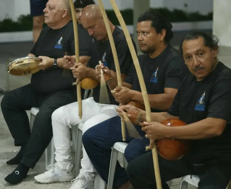 Grupo de capoeiristas sentados tocando berimbau
