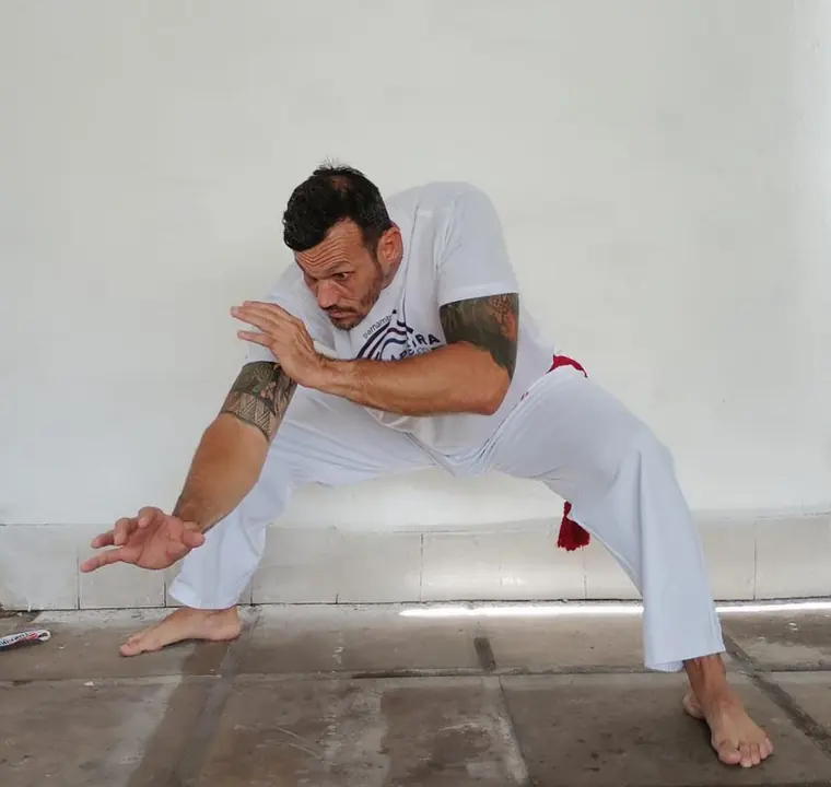 Capoeirista agachado em movimento de ginga, uniforme branco