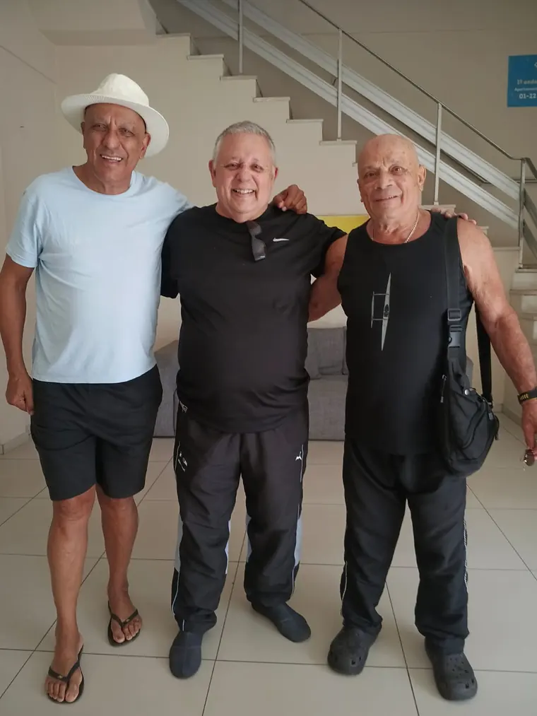 Três mestres sorrindo, um deles de chapéu, em confraternização