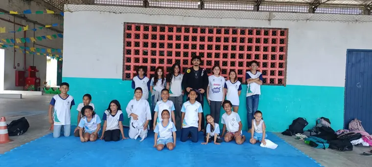 Turma de crianças uniformizadas de branco e azul no tatame da escola